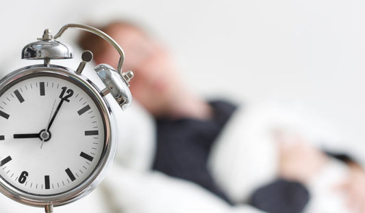 Μεταλλικό ξυπνητήρι μπροστά σε άντρα που κοιμάται στο κρεβάτι