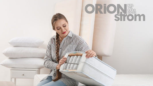 Γυναίκα εξετάζει δείγμα στρώματος ORION Strom με εμφανείς εσωτερικές στρώσεις και ελατήρια, σε φωτεινό δωμάτιο.