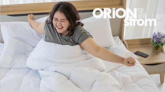 μια χαμογελαστή γυναίκα που τεντώνεται χαρούμενα στο κρεβάτι, πάνω σε λευκά σκεπάσματα, με το λογότυπο ORION Strom πάνω δεξιά.