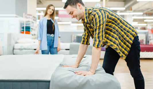 Άντρας δοκιμάζει στρώμα σε κατάστημα επίπλων ενώ γυναίκα παρακολουθεί