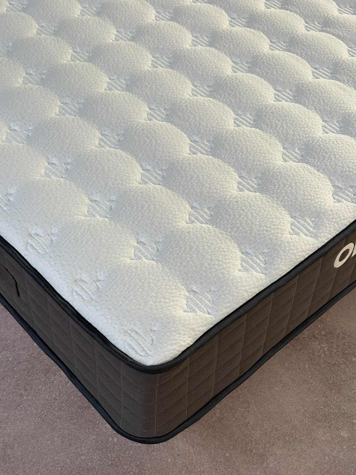 ORION ATLAS — Original close-up of the white knitted surface, showing raised quilting, fine fabric texture and small repeating motifs. Black piping and square stitching on the dark side panel are clearly visible.